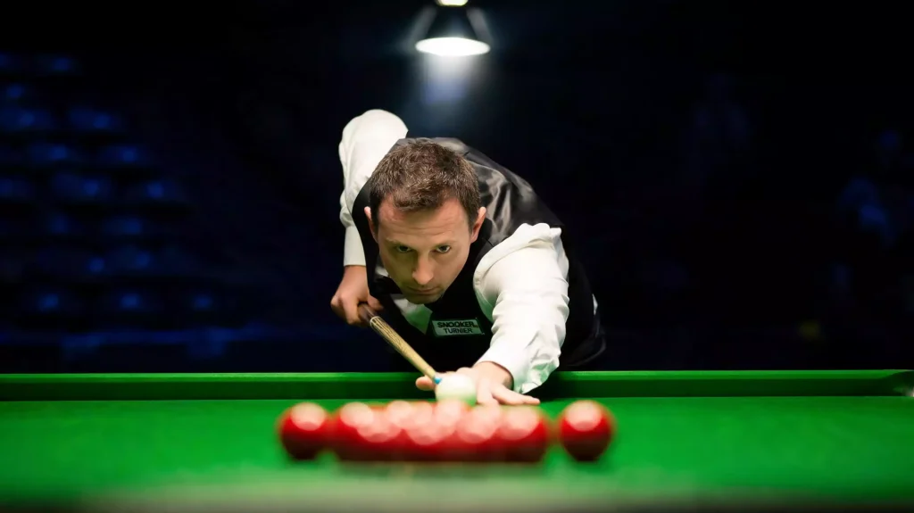 Snookerspieler im Anzug visiert konzentriert einen langen Stoß auf grünem Tuch bei der Snooker WM 2026 an